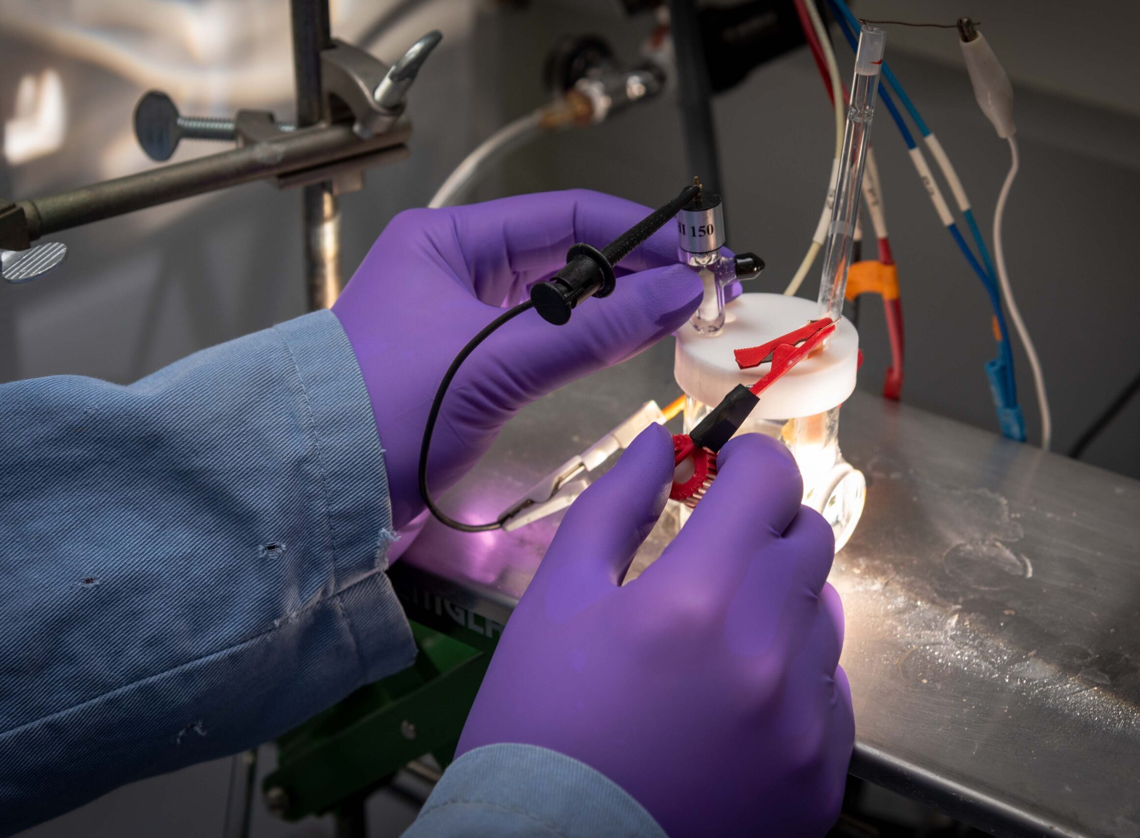 Purple-gloved hands connecting wires to a battery.