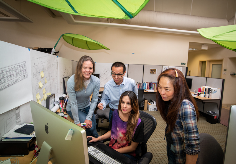 Four people gathered around a computer desk smiling