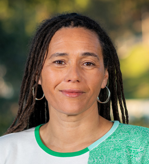 Person with long, braided dark hair wearing silver hoop earrings and a green and white shirt.