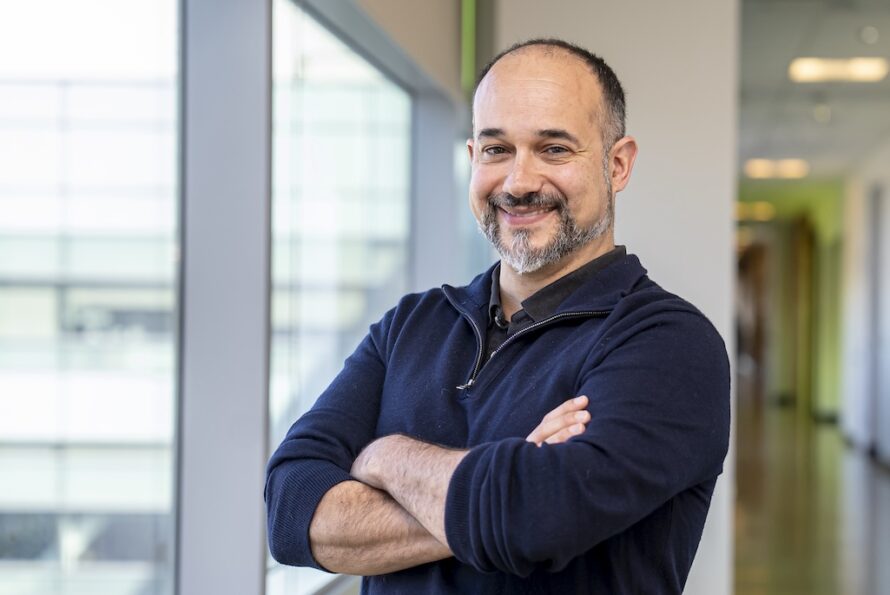 A person in a navy top standing with their arms crossed in front of a hallway.