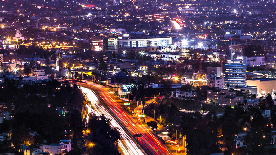 Photograph of a city at night with light shining from automobiles and buildings.