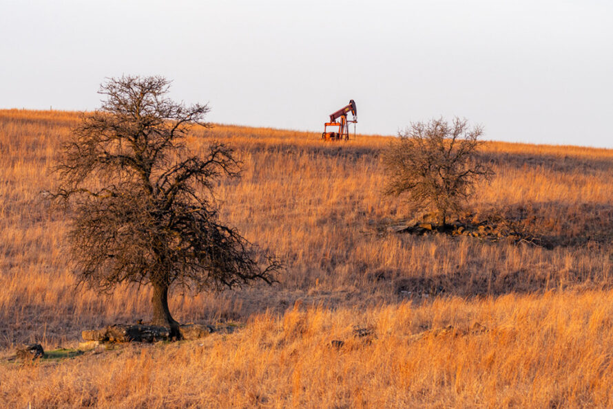 An orphaned well on a dry, grassy field. Two trees are visible in the foreground.
